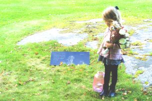Flicka med blommor och lykta vid gravplats hund